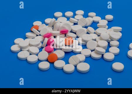 Eine Sammlung verschiedener Pillen und Tabletten, die auf einer leuchtend blauen Oberfläche verteilt sind. Ideal für medizinische und gesundheitsbezogene Visualisierungen. Stockfoto