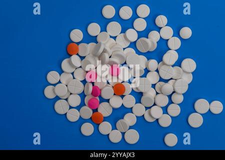 Eine Sammlung verschiedener Pillen und Tabletten, die auf einer leuchtend blauen Oberfläche verteilt sind. Ideal für medizinische und gesundheitsbezogene Visualisierungen. Stockfoto