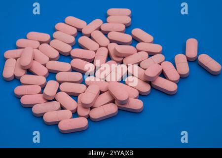 Nahaufnahme eines Stapels rosafarbener Pillen auf blauer Oberfläche, Gesundheitskonzept. Stockfoto
