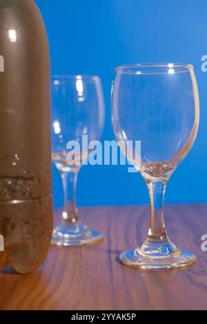 Eine stilvolle Komposition mit Gläsern und einer Flasche Wein auf einem rustikalen Holztisch vor einem leuchtend blauen Hintergrund. Perfekt zum Essen, ce Stockfoto