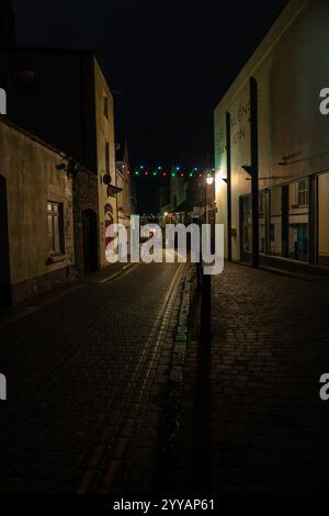 Festliche weihnachtslichter, die nachts über eine verlassene Kopfsteinpflasterstraße aufgehängt werden, schaffen eine magische Atmosphäre Stockfoto