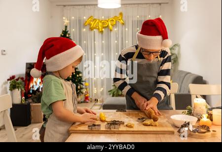 Zwei glückliche Kinder, die Weihnachtsmützen tragen und Weihnachtskekse in einer warmen, festlichen Küche zubereiten. Stockfoto