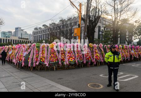 Seoul, Südkorea. Dezember 2024. Ein Polizist steht mit Kränzen, die von Anhängern des angeklagten südkoreanischen Präsidenten Yoon Suk Yeol vor dem Verfassungsgericht in Seoul geschickt wurden. Das südkoreanische Verfassungsgericht wägt seine Optionen ab, da eine Reihe von Dokumenten, mit denen das Amtsenthebungsverfahren gegen Präsident Yoon Suk Yeol eingeleitet wurde, ihm nach fünf Tagen nicht zugestellt wird, sagte ein Gerichtssprecher am 20. Dezember. Quelle: SOPA Images Limited/Alamy Live News Stockfoto