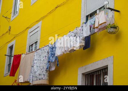 Trocknen der Kleidung vor den Fenstern an der gelben Wand. Helles, farbenfrohes Gebäude in Portugal. Traditionelles Haus in Europa. Wäscherei am Seil Stockfoto