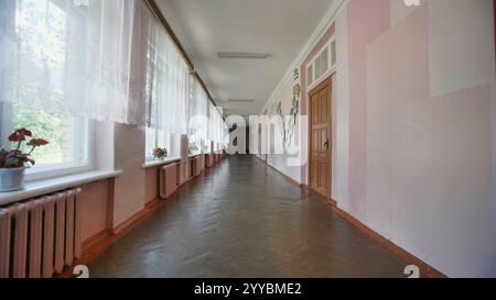Lange hinunter gehen. Leerer Schulflur am letzten Schultag. Sonnenlicht strömt durch die Fenster. Ein warmes Leuchten auf Holzböden und -Wände Stockfoto
