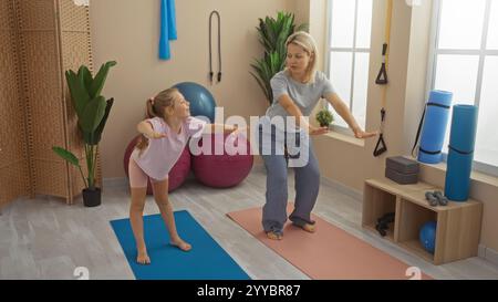 Mutter und Tochter üben gemeinsam Übungen in einem Indoor-Gymnasium mit Yogamatten und Fitnessgeräten um sie herum Stockfoto