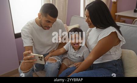 Familie genießt die gemeinsame Zeit drinnen mit einem Mann, einer Frau und einem Kind, das in einem gemütlichen Wohnzimmer auf einem Smartphone lächelt. Stockfoto