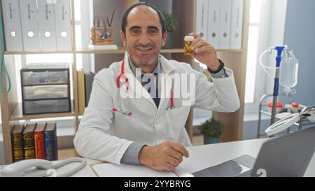 Ein reifer, hispanischer Mann mit weißem Mantel und Stethoskop, sitzt in einem Klinikbüro, hält eine verschreibungspflichtige Pillenflasche mit einem Lächeln hoch, umgeben von B Stockfoto