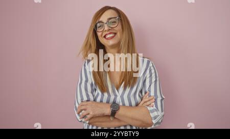 Frau mittleren Alters mit blonden Haaren und Brille, die selbstbewusst steht und vor einem pinkfarbenen Hintergrund lächelt Stockfoto