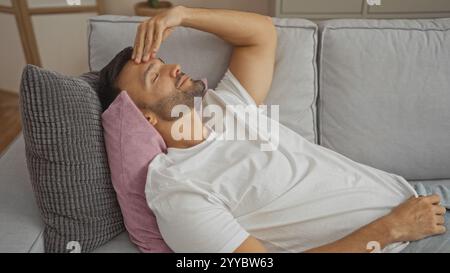Hübscher junger hispanischer Mann mit Bart, der sich auf einem Sofa in seinem Wohnzimmer zu Hause entspannt. Stockfoto
