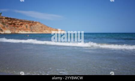 Unscharfer Blick auf einen wunderschönen Strand mit Wellen, die gegen die Küste krachen, umgeben von klarem blauem Himmel und felsigen Klippen im Hintergrund Stockfoto