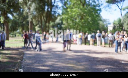 Verschwommene Menschenmenge in den Gärten der Villa borghese in rom mit defokussierten Bäumen unter blauem Himmel, die eine friedliche Atmosphäre im Freien schaffen, bei der Menschen spazieren gehen und entspannen können Stockfoto