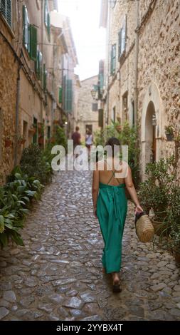 Frau, die durch eine enge Steinstraße in valldemossa, mallorca, spanien, läuft, umgeben von rustikalen Gebäuden und üppigem Grün an einem sonnigen Tag Stockfoto