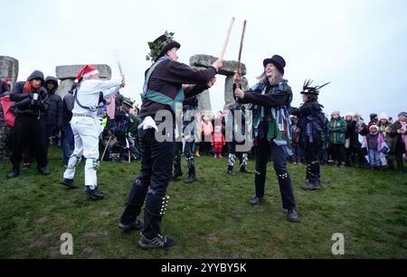 Morris-Tänzer treten vor den Steinen auf, während die Menschen während des Sonnenaufgangs am prähistorischen Monument von Stonehenge auf der Salisbury Plain in Wiltshire an der Wintersonnenwende teilnehmen. Bilddatum: Samstag, 21. Dezember 2024. Stockfoto