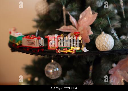 Ein entzückender kleiner Zugschmuck, der fröhlich einen wunderschön verzierten und festlichen Weihnachtsbaum umkreist Stockfoto