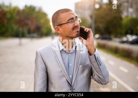 Porträt eines verzweifelten Geschäftsmannes, der am Telefon spricht. Junger Geschäftsmann, der auf der Straße steht und ein Smartphone benutzt. Stockfoto