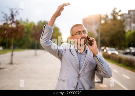 Porträt eines verzweifelten Geschäftsmannes, der am Telefon spricht. Junger Geschäftsmann, der auf der Straße steht und ein Smartphone benutzt. Stockfoto