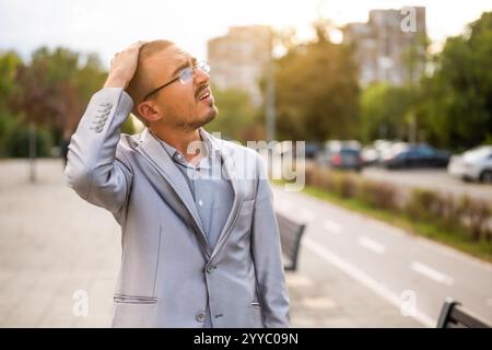 Porträt eines enttäuschten jungen Geschäftsmannes, der auf der Straße steht und denkt. Ängstlicher und nachdenklicher Geschäftsmann nach der Arbeit. Stockfoto