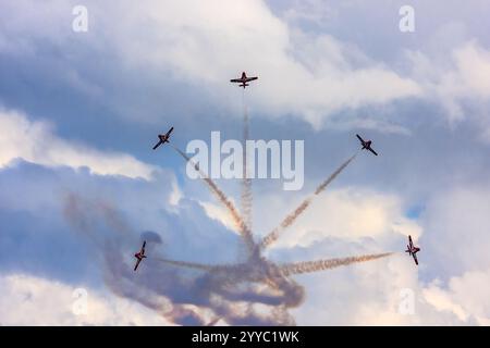 Eine Gruppe von fünf Kampfflugzeugen fliegt in Formation und hinterlässt eine Rauchspur hinter sich. Der Himmel ist bewölkt und die Sonne untergeht, was einen Drang erzeugt Stockfoto