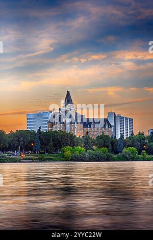 Ein wunderschöner Sonnenuntergang über einer Stadt mit einem großen Gebäude im Hintergrund. Das Wasser ist ruhig und der Himmel ist voller Wolken Stockfoto