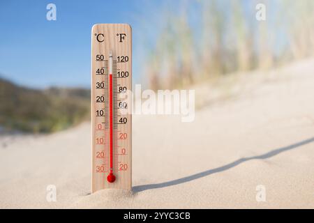 Hölzerner celsius- und fahrenheit-Skalenthermometer im Sand. Umgebungstemperatur plus 40 Grad. Heißer Sommertag Stockfoto