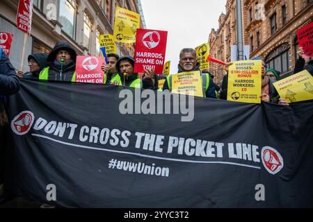 London, UK, 21. Dezember 2024. Demonstranten stehen hinter einem Protestbanner. Mitglieder der UVW union halten eine Demonstration vor dem weltberühmten Londoner Kaufhaus Harrods ab. Restaurantpersonal, Reinigungspersonal und Sicherheitsbeamte halten an einem der geschäftigsten Einkaufstage des Jahres eine Streikschlange vor dem Haupteingang. Die UVW-gewerkschaft fordert, dass ihren Mitgliedern ein versprochener Weihnachtsbonus, eine Erhöhung der Regellöhne und eine Verbesserung der allgemeinen Arbeitsbedingungen gezahlt wird. Quelle: James Willoughby/ALAMY Live News Stockfoto