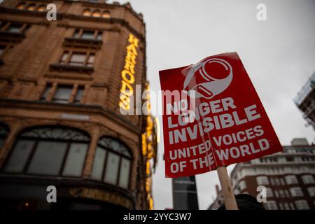 London, UK, 21. Dezember 2024. Ein Protestplakat ist vor dem beleuchteten Harrods-Schild angebracht. Mitglieder der UVW union halten eine Demonstration vor dem weltberühmten Londoner Kaufhaus Harrods ab. Restaurantpersonal, Reinigungspersonal und Sicherheitsbeamte halten an einem der geschäftigsten Einkaufstage des Jahres eine Streikschlange vor dem Haupteingang. Die UVW-gewerkschaft fordert, dass ihren Mitgliedern ein versprochener Weihnachtsbonus, eine Erhöhung der Regellöhne und eine Verbesserung der allgemeinen Arbeitsbedingungen gezahlt wird. Quelle: James Willoughby/ALAMY Live News Stockfoto