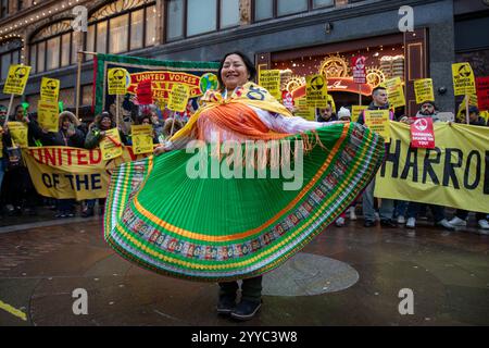 London, UK, 21. Dezember 2024. Ein Demonstrant tanzt vor Demonstranten mit Schildern. Mitglieder der UVW union halten eine Demonstration vor dem weltberühmten Londoner Kaufhaus Harrods ab. Restaurantpersonal, Reinigungspersonal und Sicherheitsbeamte halten an einem der geschäftigsten Einkaufstage des Jahres eine Streikschlange vor dem Haupteingang. Die UVW-gewerkschaft fordert, dass ihren Mitgliedern ein versprochener Weihnachtsbonus, eine Erhöhung der Regellöhne und eine Verbesserung der allgemeinen Arbeitsbedingungen gezahlt wird. Quelle: James Willoughby/ALAMY Live News Stockfoto