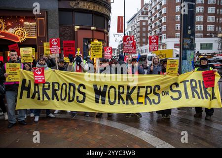 London, UK, 21. Dezember 2024. Demonstranten stehen hinter einem Protestbanner. Mitglieder der UVW union halten eine Demonstration vor dem weltberühmten Londoner Kaufhaus Harrods ab. Restaurantpersonal, Reinigungspersonal und Sicherheitsbeamte halten an einem der geschäftigsten Einkaufstage des Jahres eine Streikschlange vor dem Haupteingang. Die UVW-gewerkschaft fordert, dass ihren Mitgliedern ein versprochener Weihnachtsbonus, eine Erhöhung der Regellöhne und eine Verbesserung der allgemeinen Arbeitsbedingungen gezahlt wird. Quelle: James Willoughby/ALAMY Live News Stockfoto