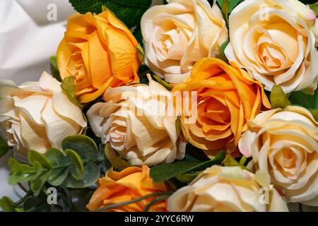 Ein lebendiger Haufen künstlicher Rosen zeigt Gelb- und Cremetönen, die wunderschön zwischen Grün angeordnet sind. Perfekt für jedes dekorative Spa Stockfoto