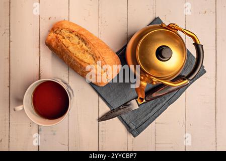 Eine goldfarbene Teekanne aus Aluminium, eine Porzellanpfanne und -Tasse, ein Messer und ein blaues Tuch. Stockfoto