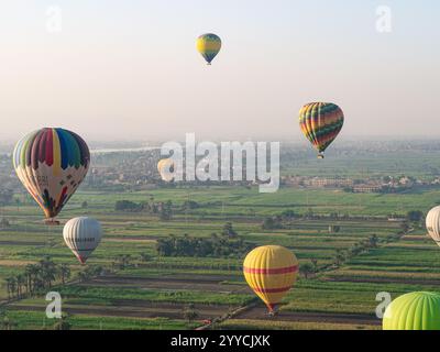 Heißluftballons fliegen über das Tal der Könige, Luxor, Ägypten mit grünen Feldern im Niltal als Kulisse 2 Stockfoto