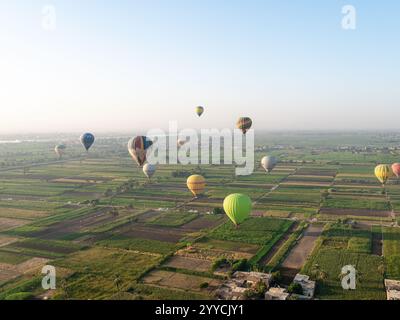 Heißluftballons fliegen über das Tal der Könige in Luxor, Ägypten mit grünen Feldern im Niltal als Kulisse Stockfoto