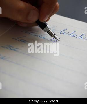 Darstellung einer linken Hand eines Kindes, die die Silben li und le mit einem Füllfederhalter in ein Copybook schreibt. Konzept zum Schreiben mit der linken Hand. Zurück zur Schule Stockfoto