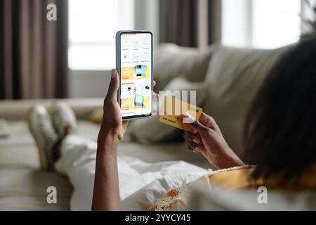 Nicht erkennbare Frau, die auf der Couch liegt, während sie ihr Smartphone zum Online-Shopping benutzt Stockfoto