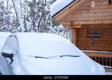 Finnisch Lappland im Winter. Schneebedecktes Auto vor einem Holzhaus im verschneiten Wald Stockfoto