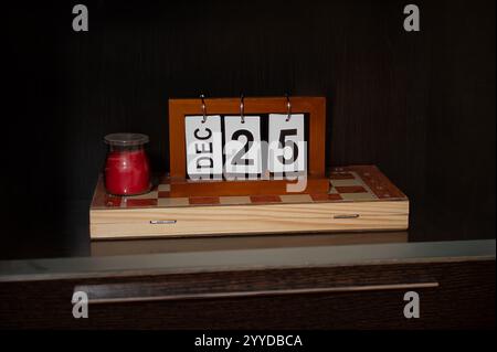 Das Bild zeigt einen Holzblock-Kalender, der den 25. Dezember als Symbol für Weihnachten zeigt, neben einer kleinen roten Kerze, die alle auf einem dekorativen Arbeitsauftrag platziert sind Stockfoto