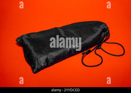 Eine elegante, schwarze Aufbewahrungstasche liegt flach vor einem leuchtenden orangefarbenen Hintergrund. Der Kordelzug weist auf Funktionalität für verschiedene Aufbewahrungszwecke hin Stockfoto
