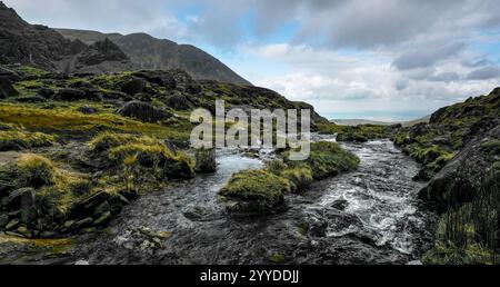 Ein kleiner Fluss durchquert eine bergige Landschaft. Das Wasser ist relativ flach und fließend. Stockfoto
