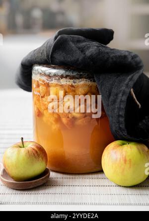 Machen Sie Ihren eigenen Apfelessig zu Hause, fermentieren Sie geschnittene Äpfel in einem Glasgefäß, der mit einem dunklen Leinentuch bedeckt ist. In Bearbeitung. Stockfoto