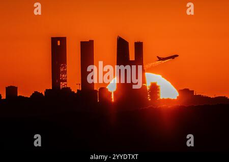Madrid, Spanien. Dezember 2024. Die Sonne untergeht während der Wintersonnenwende über der Skyline mit den Wolkenkratzern des Geschäftsviertels von Madrid, während ein Flugzeug vom Flughafen Adolfo Suarez Madrid Barajas startet. Die Wintersonnenwende ist der Tag mit der kürzesten Zeit des Tageslichts und der längsten Nacht des Jahres. Quelle: Marcos del Mazo/Alamy Live News Stockfoto