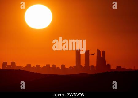 Madrid, Spanien. Dezember 2024. Die Sonne untergeht während der Wintersonnenwende über der Skyline mit den Wolkenkratzern des Geschäftsviertels von Madrid, während ein Flugzeug vom Flughafen Adolfo Suarez Madrid Barajas startet. Die Wintersonnenwende ist der Tag mit der kürzesten Zeit des Tageslichts und der längsten Nacht des Jahres. Quelle: Marcos del Mazo/Alamy Live News Stockfoto