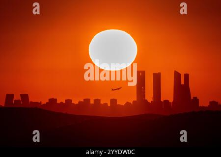 Madrid, Spanien. Dezember 2024. Die Sonne untergeht während der Wintersonnenwende über der Skyline mit den Wolkenkratzern des Geschäftsviertels von Madrid, während ein Flugzeug vom Flughafen Adolfo Suarez Madrid Barajas startet. Die Wintersonnenwende ist der Tag mit der kürzesten Zeit des Tageslichts und der längsten Nacht des Jahres. Quelle: Marcos del Mazo/Alamy Live News Stockfoto