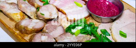 Eine wunderschön arrangierte Auswahl an Wurstwaren auf einem Holzbrett, zusammen mit einer lebendigen Dip-Sauce und garniert mit frischen grünen Zwiebeln, evoki Stockfoto