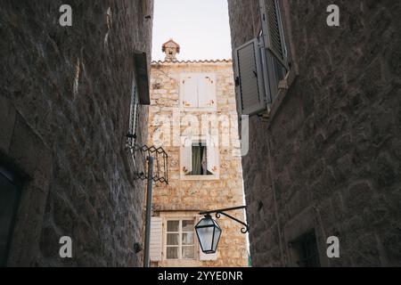 Malerischer Blick auf eine enge Kopfsteinpflasterstraße, die zu einem traditionellen Steinhaus mit offenen Fenstern führt und die charmante Architektur von budva, Stockfoto