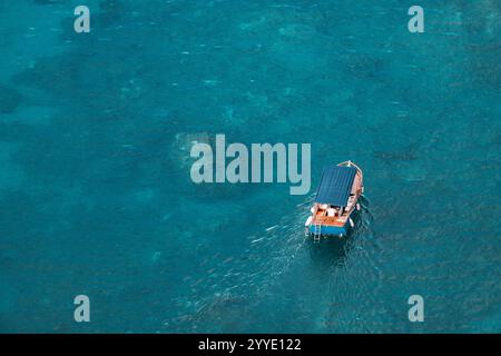 Aus der Vogelperspektive eines kleinen Touristenbootes, das auf einer ruhigen türkisfarbenen Wasseroberfläche segelt Stockfoto