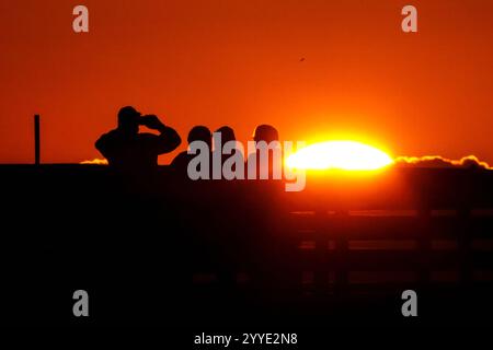 Isle Of Palms, Usa. Dezember 2024. Eine Gruppe von Menschen beobachtet den Sonnenaufgang an einem kalten Morgen zur Wintersonnenwende vom Isle of Palms Pier, 21. Dezember 2024 in Isle of Palms, South Carolina. Die Wintersonnenwende ist der kürzeste Tag der nördlichen Hemisphäre und markiert den Beginn des Winters. Quelle: Richard Ellis/Richard Ellis/Alamy Live News Stockfoto