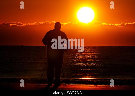 Isle Of Palms, Usa. Dezember 2024. Ein Fotograf fotografiert den Sonnenaufgang an einem kalten Morgen zur Wintersonnenwende vom Isle of Palms Pier, 21. Dezember 2024 in Isle of Palms, South Carolina. Die Wintersonnenwende ist der kürzeste Tag der nördlichen Hemisphäre und markiert den Beginn des Winters. Quelle: Richard Ellis/Richard Ellis/Alamy Live News Stockfoto