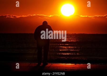 Isle Of Palms, Usa. Dezember 2024. Ein Fotograf fotografiert den Sonnenaufgang an einem kalten Morgen zur Wintersonnenwende vom Isle of Palms Pier, 21. Dezember 2024 in Isle of Palms, South Carolina. Die Wintersonnenwende ist der kürzeste Tag der nördlichen Hemisphäre und markiert den Beginn des Winters. Quelle: Richard Ellis/Richard Ellis/Alamy Live News Stockfoto