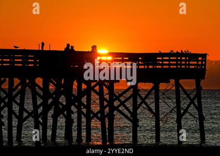 Isle Of Palms, Usa. Dezember 2024. Eine Gruppe von Menschen beobachtet den Sonnenaufgang an einem kalten Morgen zur Wintersonnenwende vom Isle of Palms Pier, 21. Dezember 2024 in Isle of Palms, South Carolina. Die Wintersonnenwende ist der kürzeste Tag der nördlichen Hemisphäre und markiert den Beginn des Winters. Quelle: Richard Ellis/Richard Ellis/Alamy Live News Stockfoto